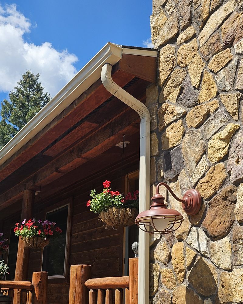 White downspout beside a stone wall and front porch