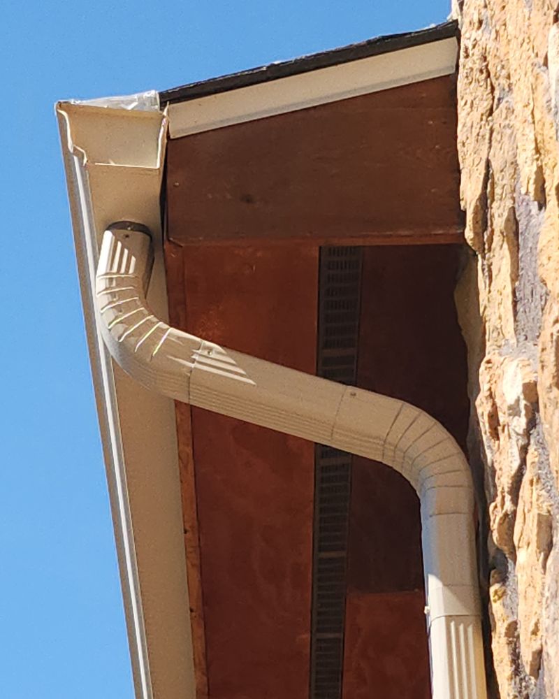 White downspout elbow under a roof eave
